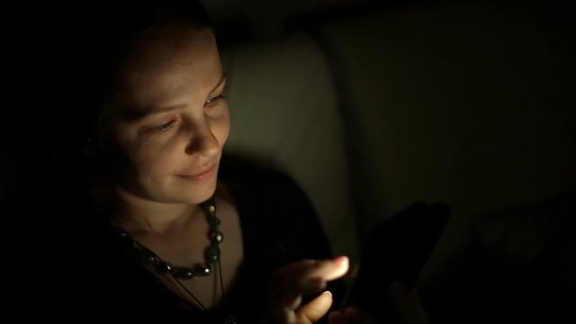a middle-aged Caucasian woman sitting at night in a room on the couch with a smartphone and communicates with friends on social networks