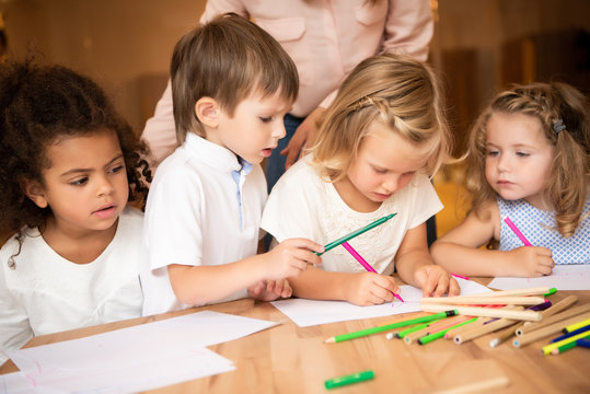 cropped image of educator standing near multicultural kids drawing in kindergarten