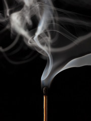 Smoking matchstick, just extinguished, on dark background