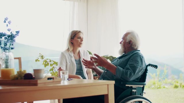 Health visitor with stethoscope and a senior man in wheelchair at home, talking.