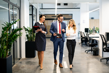 Full length of group of happy young business people walking the corridor in office together