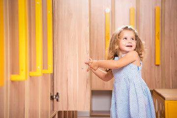 smiling adorable kid opening locker in kindergarten cloakroom