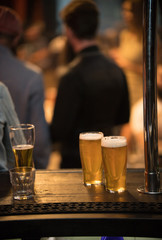 Mugs with beer and a glass of alcohol stand on the table on the background with people