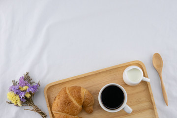 A cup of coffee, milk and croissant with statice flower bouquet on white bed with copy space