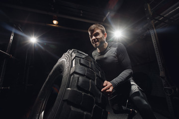 Fototapeta na wymiar Muscular fitness man flipping tire wheel. Concept lifting, workout training.