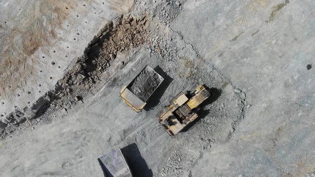 4k Aerial view of a close-up dump truck loading iron ore into a truck on a quarried quarry
