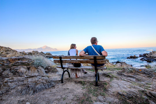 Halkidiki, Greece. Married couple sit at bench watching sea and think positively