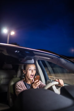 Young female driver playing with her cellphone instead of paying attention to driving startled in a potentially dangerous situation - Road safety concept