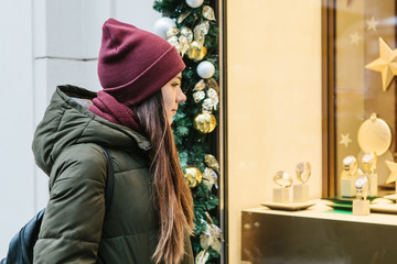 A young beautiful woman or girl looks at the shop window and chooses a Christmas gift.