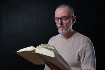 old man with glasses reading a book