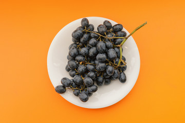 Dark grapes in plate on orange background.