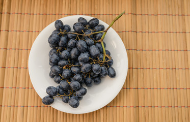 Dark grapes in plate on wooden background.