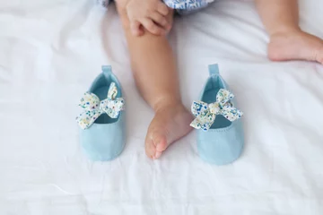 Small light blue baby shoes with floral bows around the little child leg © Анна В