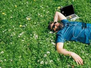 Tired freelancer lying on grass near his laptop computer