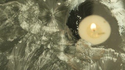 Burning candle in the background of a window with ice flowers - Powered by Adobe