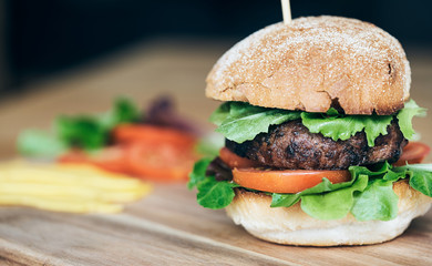 A beef burger in a crusty bun with lettuce and tomatoes on a cho