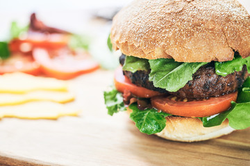 A beef burger in a crusty bun with lettuce and tomatoes on a cho