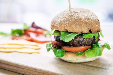 A beef burger in a crusty bun with lettuce and tomatoes on a cho