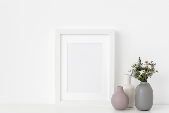White A5 portrait frame mockup with composition of small vases and dried flowers on white wall background. Empty frame, poster mock up for presentation design. 