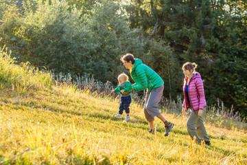 Fototapeta premium Family, childhood, fatherhood, leisure and people concept - happy father, mother and little toddler son playing and having fun outdoors over nature mountains autunmn background.