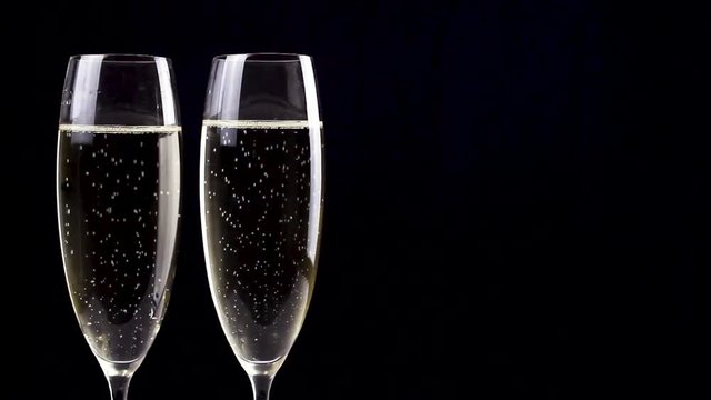 Two glasses of champagne rotating on black background.