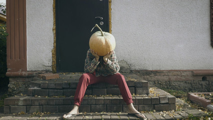 Portrait of sad pumpkin-head female sitting on the porch of an old house. Disappointed person with...