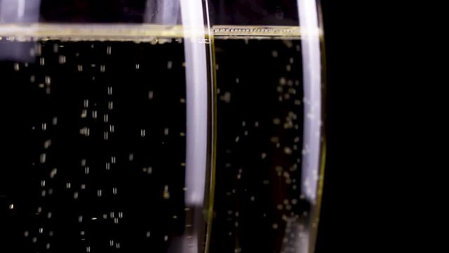 Two glasses of champagne rotating on black background.