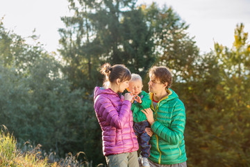Fototapeta premium Family, childhood, fatherhood, leisure and people concept - happy father, mother and little toddler son playing and having fun outdoors over nature park fall autunmn background.