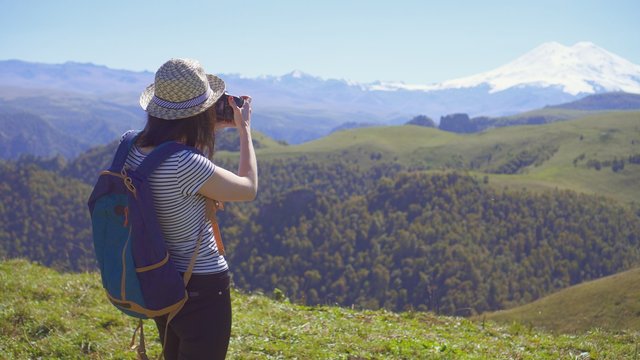 girl tourist in a hat taking pictures of beautiful mountains