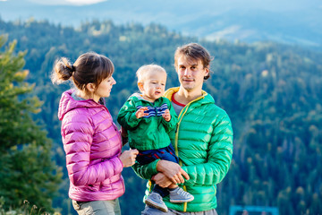 Family, childhood, fatherhood, leisure and people concept - happy father, mother and little toddler son playing and having fun outdoors over nature mountains autunmn background.