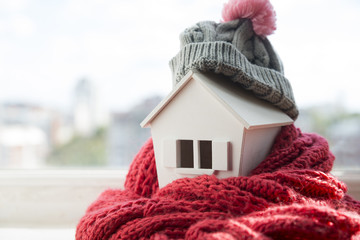 house in winter - heating system concept and cold snowy weather with model of a house wearing a...