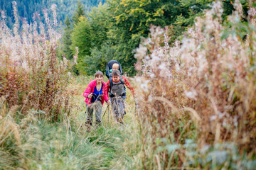 Couple hiking with baby boy travelling in backpack. Hikers family, adventure with child on autumn family trip in mountains. Vacations journey with toddler carried on back, weekend travel concept.