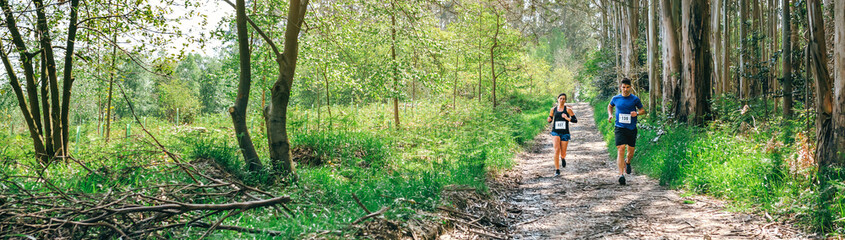 Young woman and man participating in a trail race through the forest