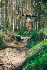 Naklejka premium Young woman jumping participating in a trail race through the forest