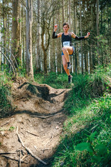 Young woman jumping participating in a trail race through the forest