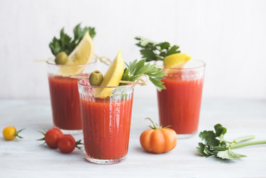 Glasses of fresh spicy tomato juice with celery garnished with lemon slice, green olive and parsley