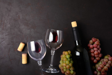 Wineglasses with red wine, bottle, grapes and corks lying on dark wooden background. Top view. Flat lay. Copy space