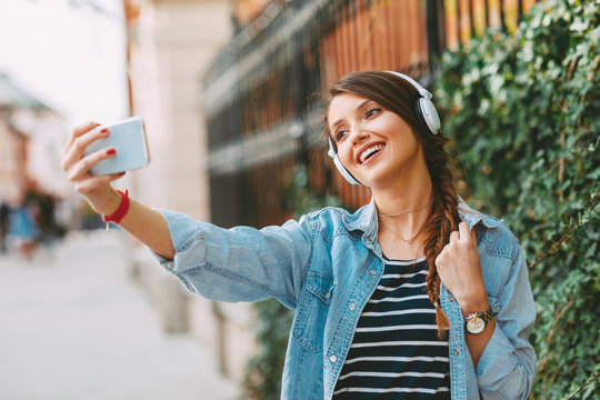 Young woman listens to music via headphones and smartphone in the city