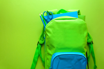 Back to school concept. Green backpack with school supplies on green background. Top view. Copy space