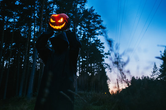 A black man in hands holds a Helluin pumpkin in a dark forest
