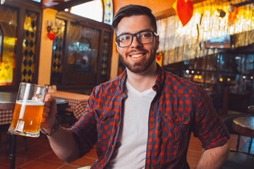 Young attractive guy in glasses with a glass of frothy beer in his hand