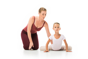 Obraz na płótnie Canvas focused female trainer helping little ballerina stretching isolated on white background