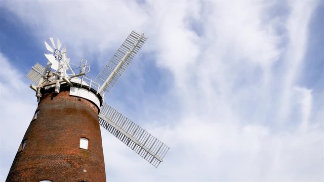 Old English Windmill. A low angle view of a traditional old English windmill in a gentle breeze set against a cloudy blue sky with space for copy.