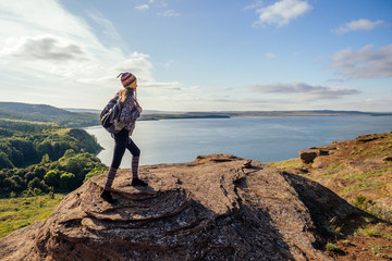 Woman in a funny hat from Nepal mountain Hiker with backpack hike walking on orange huge stones landscape lake and hills in Russia