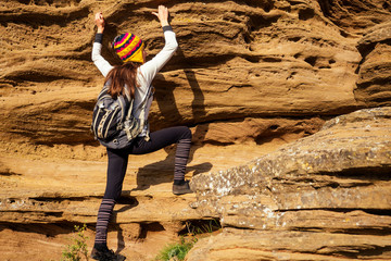 Beautiful slim and sporty young tourist woman in a funny hat from Nepal wool yak climbing big rock climbs on boulders canyon stones