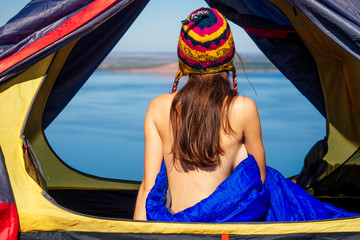Back view of sexy naked woman tourist in a funny hat from Nepal sitting in blue sleeping bag in a...