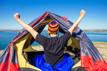 portrait of stylish ginger red-haired beard tourist man in a colorful hat made of yak wool from Nepal morning stretching warm-up in tent wrapped sleeping bag the background lake.success and freedom