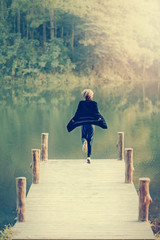 Fototapeta na wymiar woman jumping on the wooden bridge of the lake