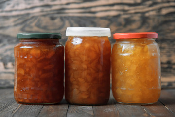 Three jars with jam on a brown wooden background.