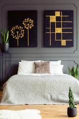 Black and gold posters above bed in grey bedroom interior with fur and plants. Real photo